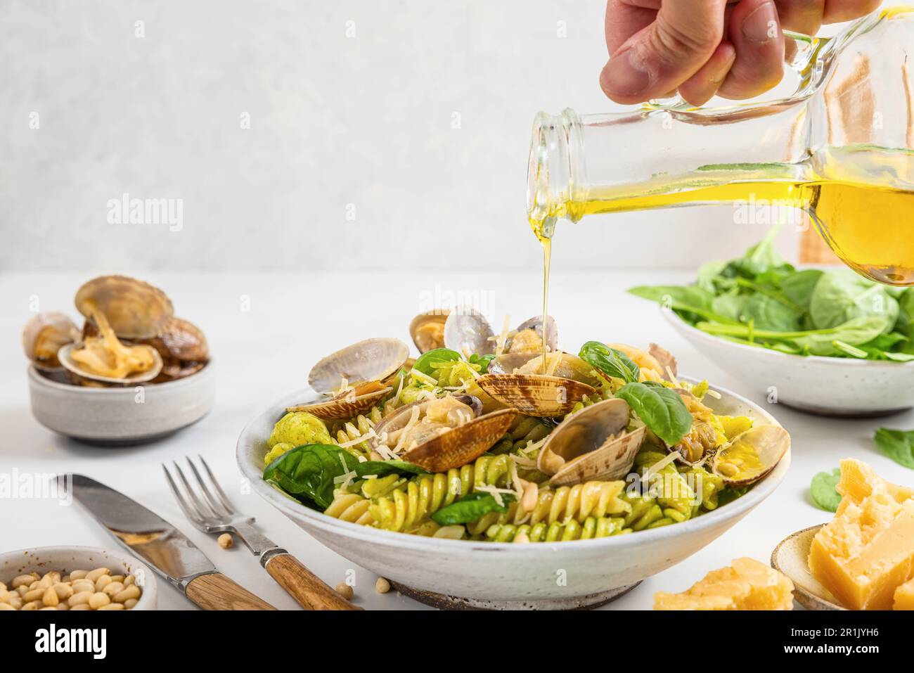 Versare l'olio d'oliva in pasta di pesce con vongole di vongole di vongole, parmigiano, spinaci, pinoli. Cucina italiana Foto Stock
