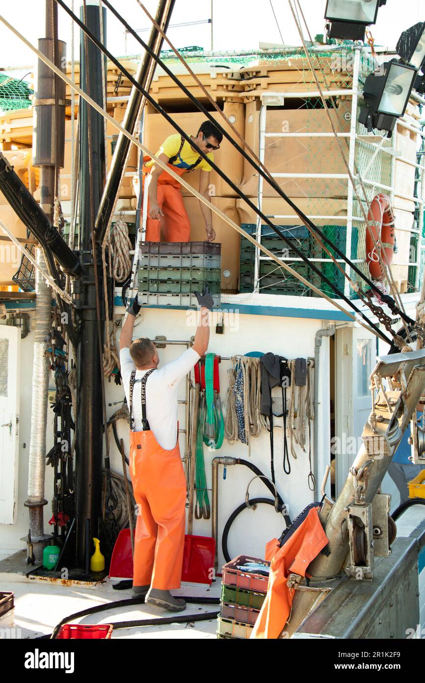 Tribunj, Croazia - 3 agosto 2022: Pescatori che mettono in ordine contenitori di plastica vuoti su un ponte di barche da pesca Foto Stock
