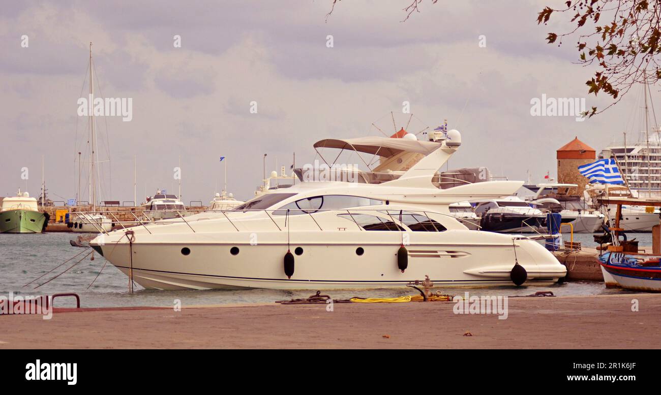 Mulini in pietra medievali con tetti rossi nel porto di Rodi. Gli yacht a motore e a vela sono ormeggiati sul terrapieno, in Mandraki Bay.Greek bandiera su una nave Foto Stock