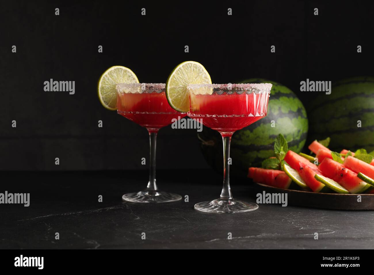 Bicchieri da cocktail di delizioso succo di cocomero fresco con lime e zucchero sul tavolo nero Foto Stock
