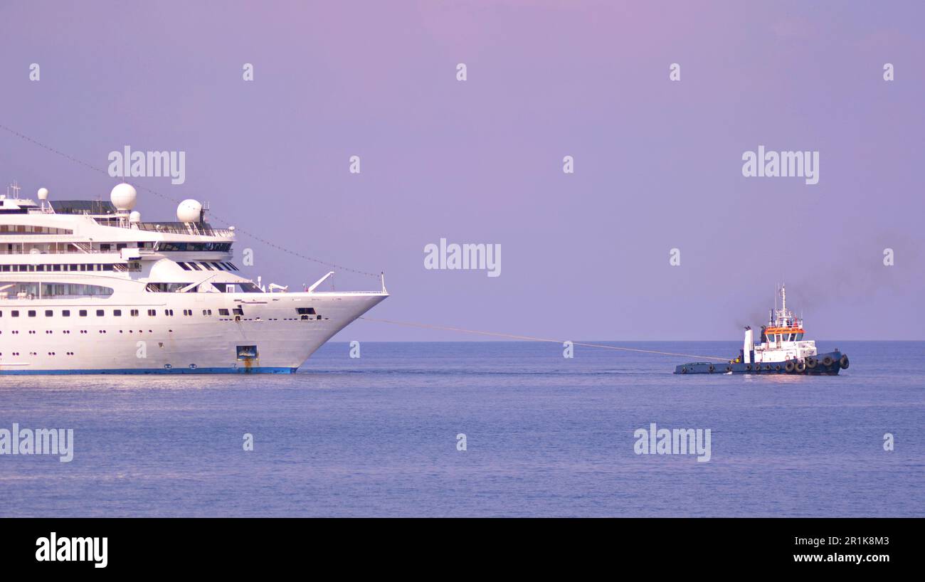 Navi, navi da crociera, barche da diporto sono ormeggiate nel porto dell'isola greca. Più piani liners. Trattore marino tira la liner. Foto Stock