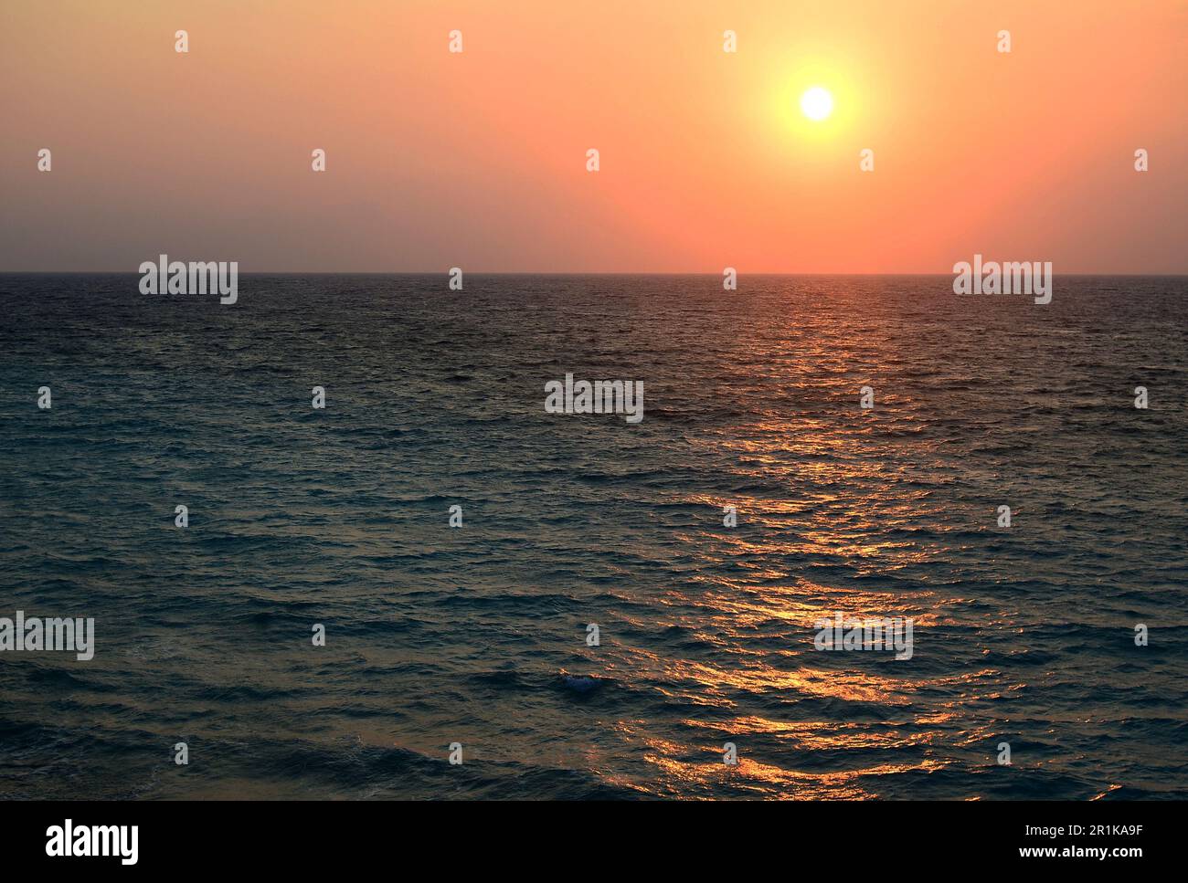 Onde di mare e il tramonto del sole all'orizzonte. I raggi gialli del sole riflessi nell'acqua di mare Foto Stock