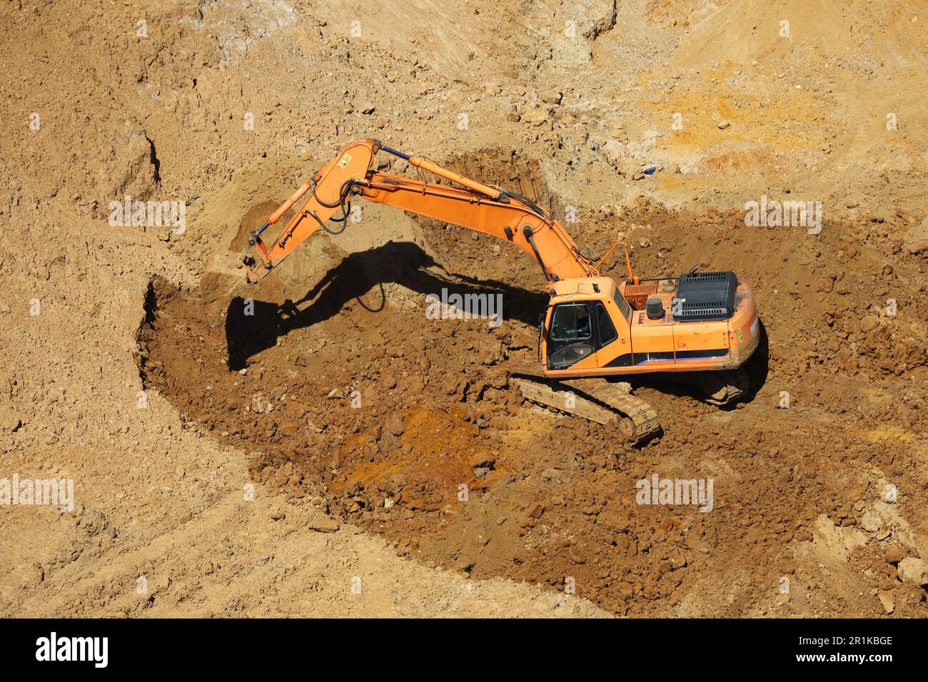 L'escavatore cingolato scarta il terreno con una benna, vista dall'alto. Lavori di movimento terra che scavano in un cantiere Foto Stock