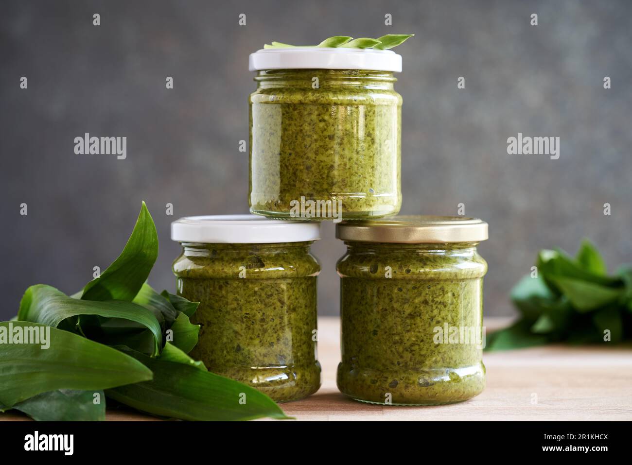 Tre vasetti di pesto all'aglio selvatico su un tavolo con foglie fresche di ursinum di Allium Foto Stock