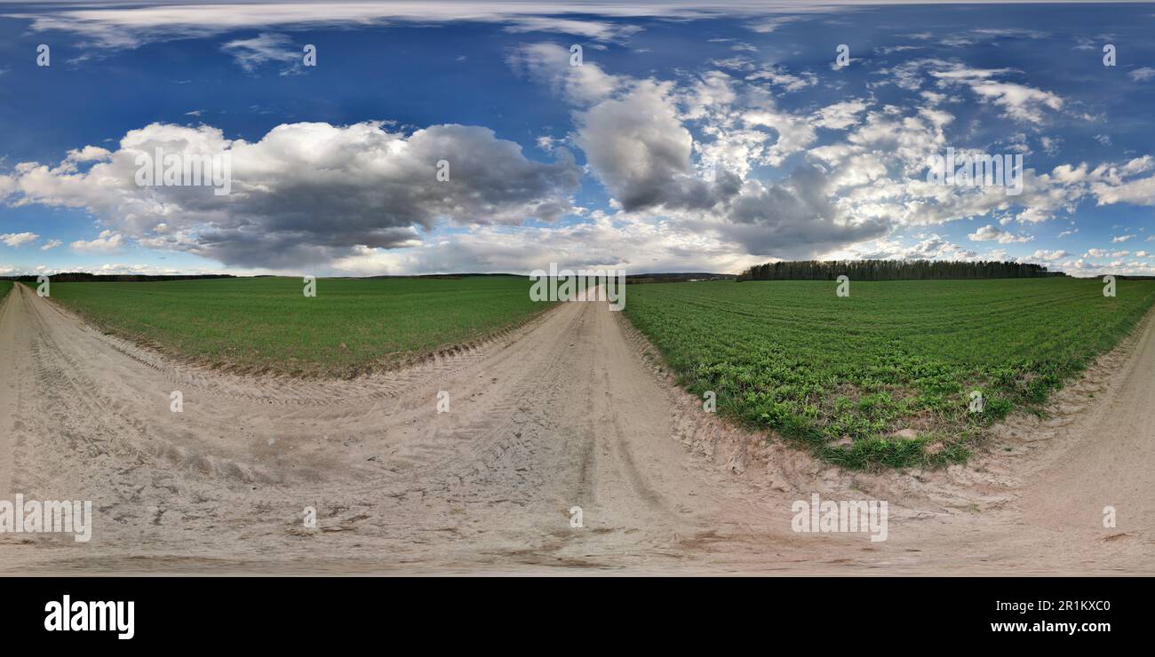 panorama sferico hdri completamente senza cuciture angolo di 360 gradi sulla strada di ghiaia rurale tra i campi in primavera giorno con le nubi impressionante in pr equirettangolare Foto Stock