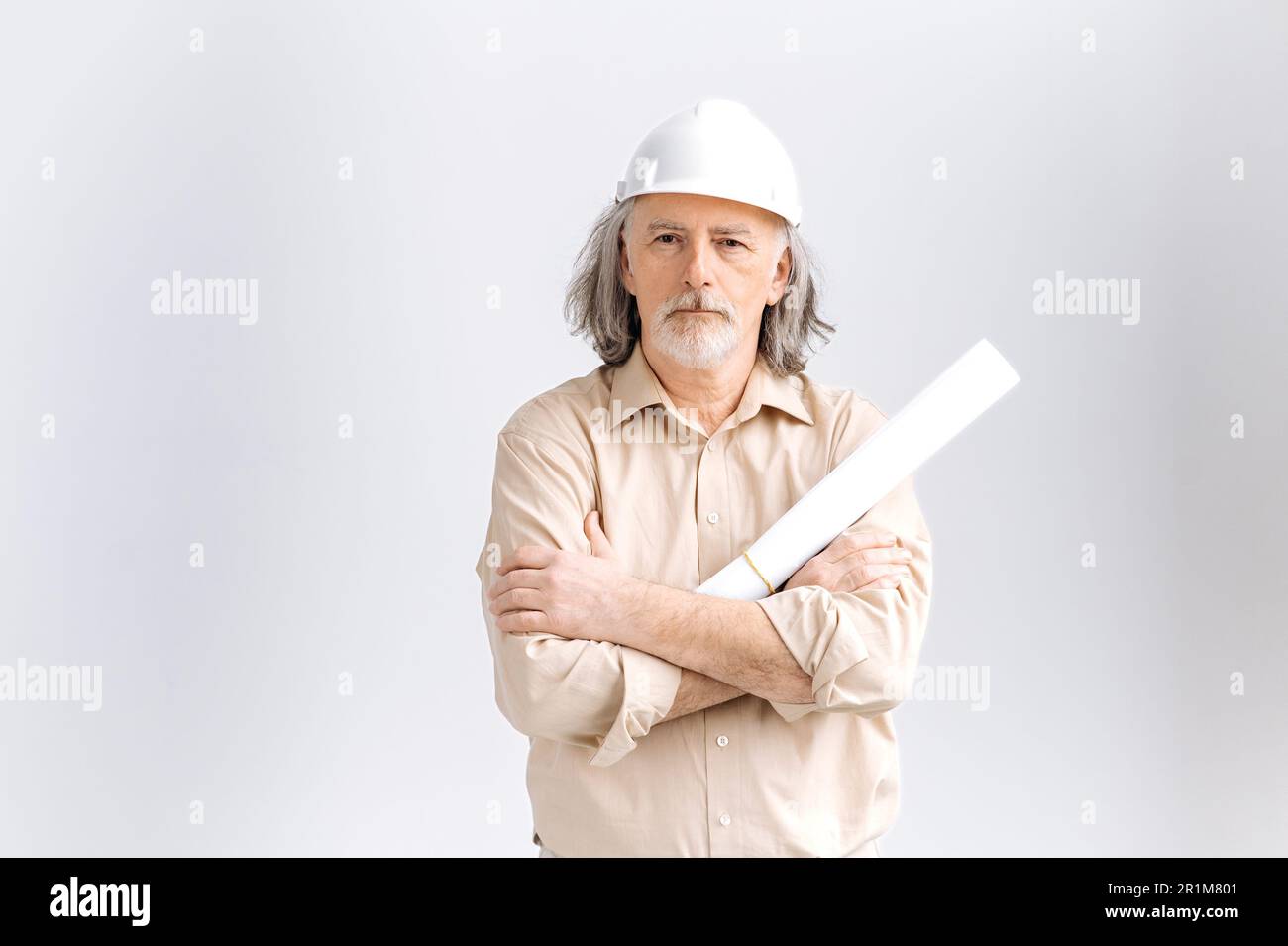 Professionista uomo maturo grigio caucasico con capelli, caposquadra, architetto lavoratore di costruzione in elmetto bianco che tiene il piano architettonico in costruzione, in piedi su sfondo bianco isolato Foto Stock
