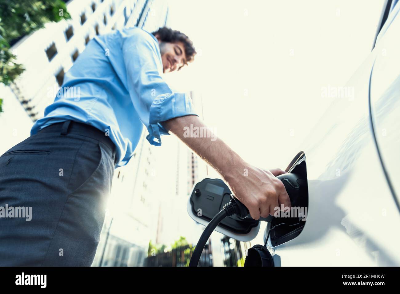 Fisheye vista mettere a fuoco sulla mano inserire il caricabatterie EV spina in auto elettrica con sfondo sfocato di progressive città moderno stile di vita-uomo d'affari ricaricare la sua Foto Stock