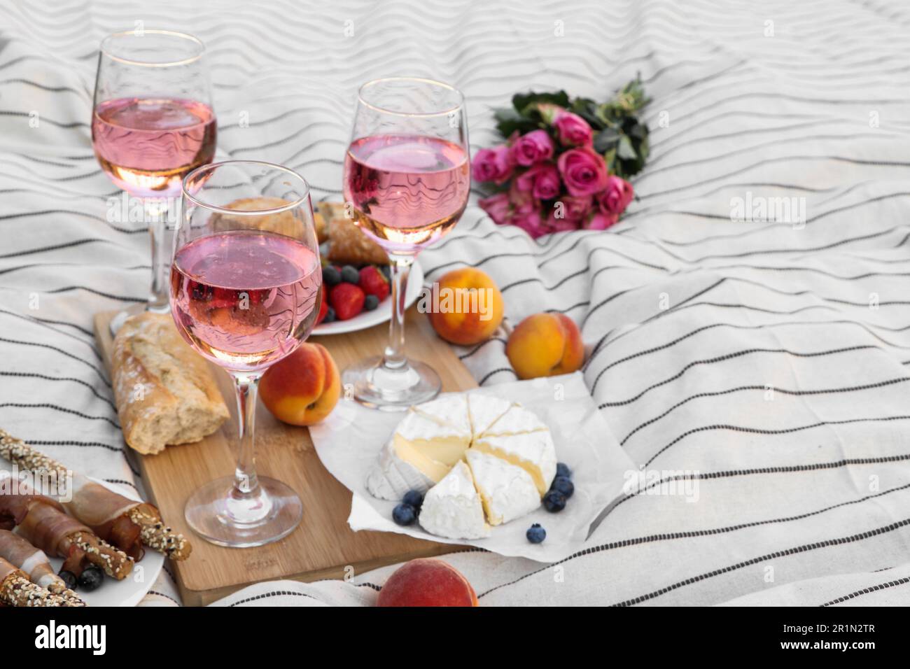 Bicchieri di delizioso vino rosa, fiori e cibo su coperta bianca da picnic Foto Stock