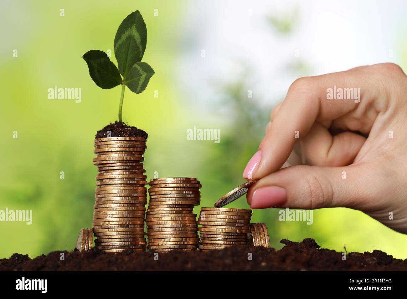 Donna che mette la moneta su pila con germoglio verde sul terreno contro sfondo sfocato, primo piano. Concetto di investimento Foto Stock