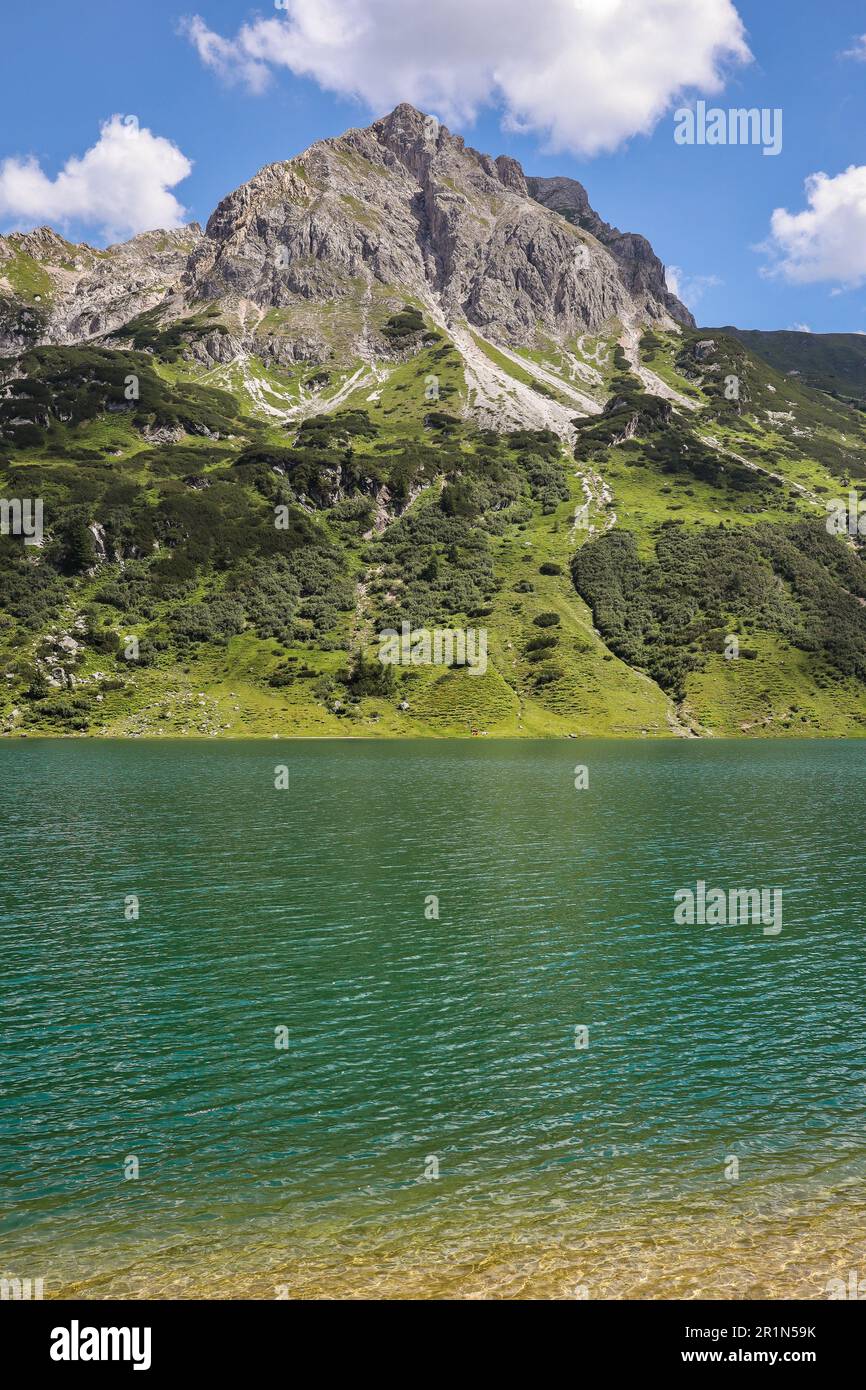 Vista verticale della splendida Rocky Peak su una collina verde con il lago alpino. Tappenkarsee con una montagna durante il giorno d'estate in Austria. Foto Stock