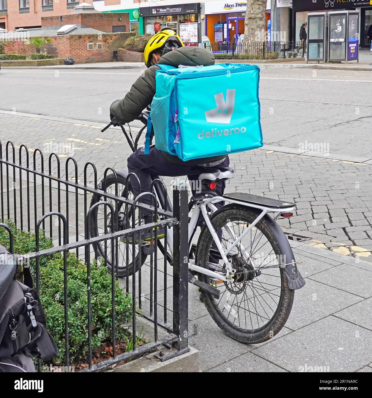 Vista sul retro, giovane ragazzo parcheggiato su una pedalata con uno zaino Deliveroo blu contenente ordini di consegna online di cibo che controllano il suo percorso Essex Inghilterra Regno Unito Foto Stock