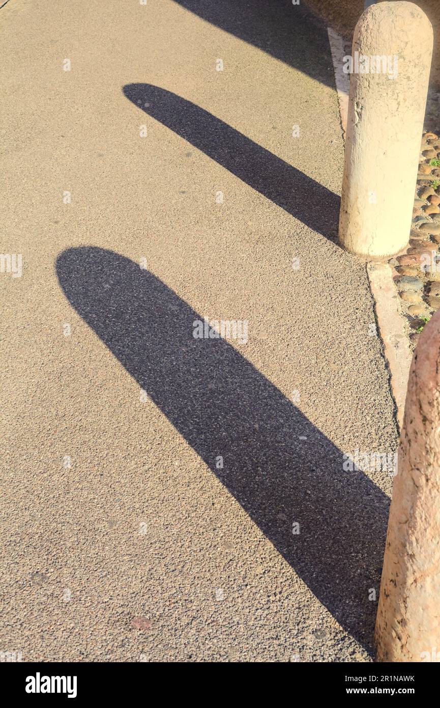 Ombre arroccate da colonne di pietra su un marciapiede al tramonto Foto Stock