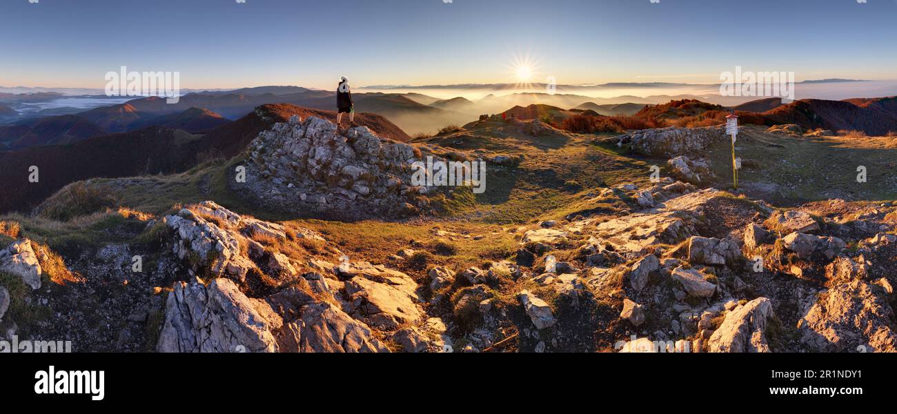 Alba con inversione sopra la profonda valle autunnale delle montagne con piccolo uomo in cima, che sta guardando questo bellissimo paesaggio Foto Stock