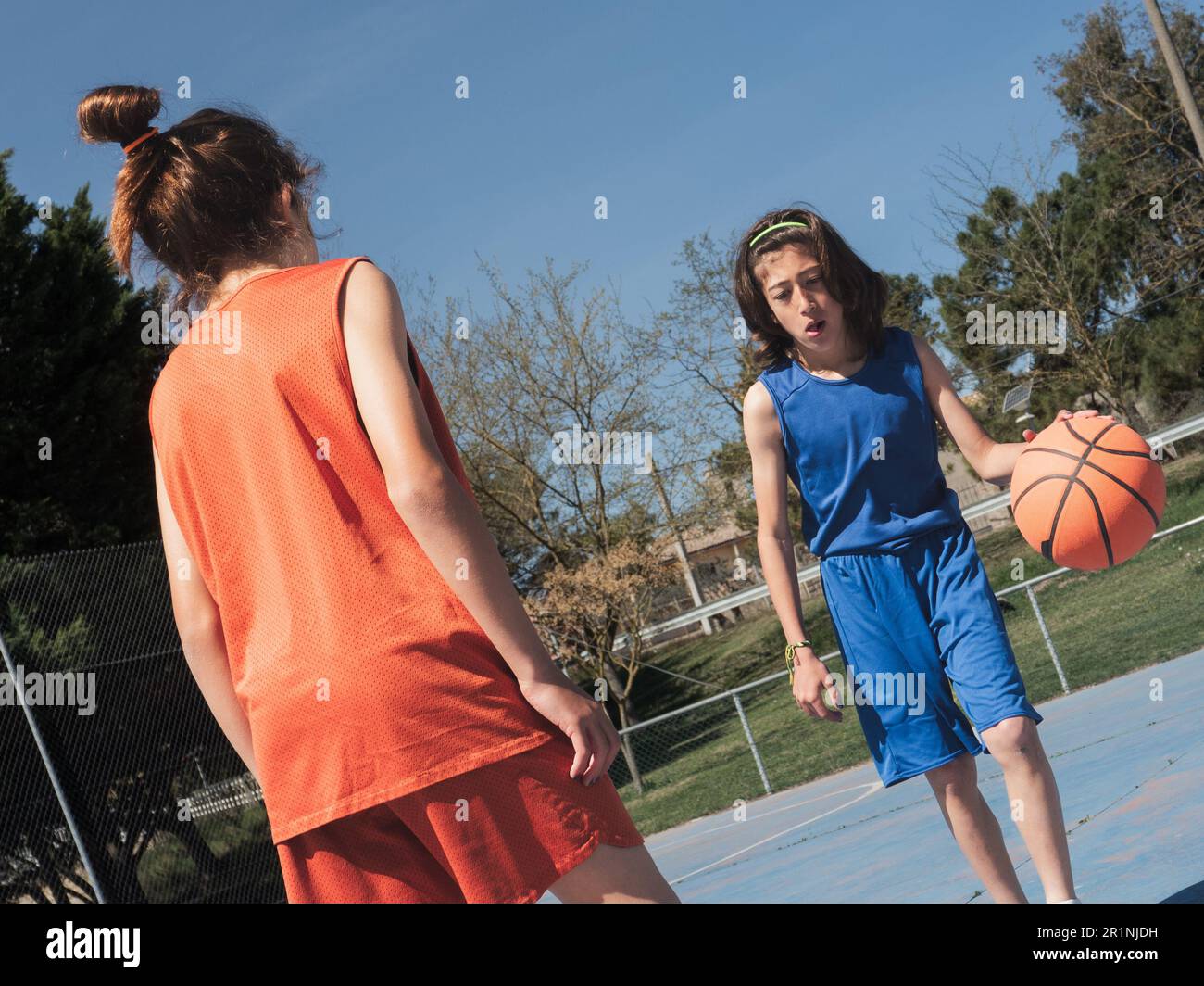 Uno a uno tra due giovani giocatori di basket in un campo all'aperto in una giornata di sole. In questa foto vediamo la competitività tra fratelli e sorelle. Foto Stock