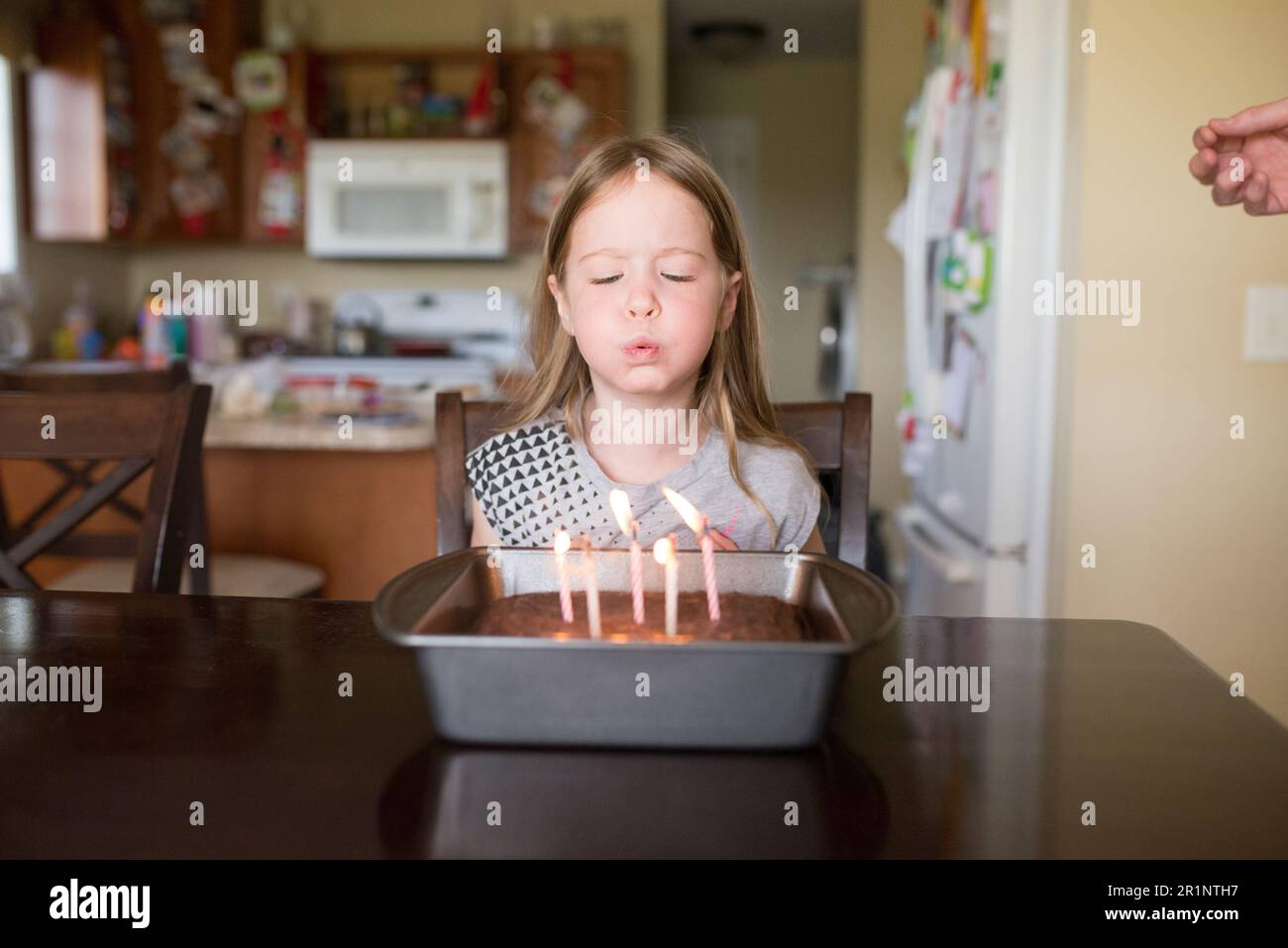 la ragazza di 5 anni soffia le candele sulla torta di compleanno a casa in cucina Foto Stock