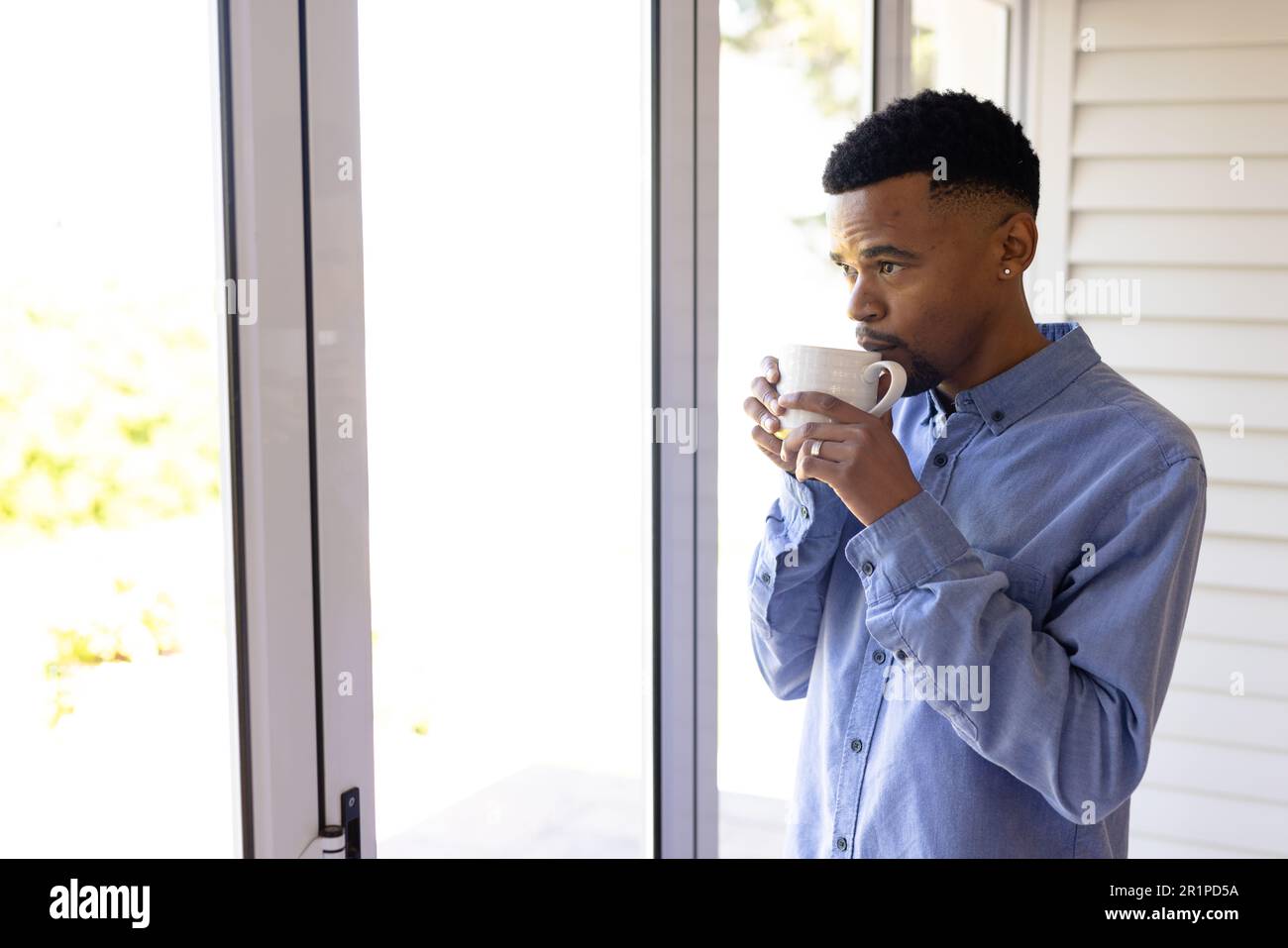 Giovane afro-americano vestito di formali bevendo caffè e guardando attraverso la finestra a casa Foto Stock