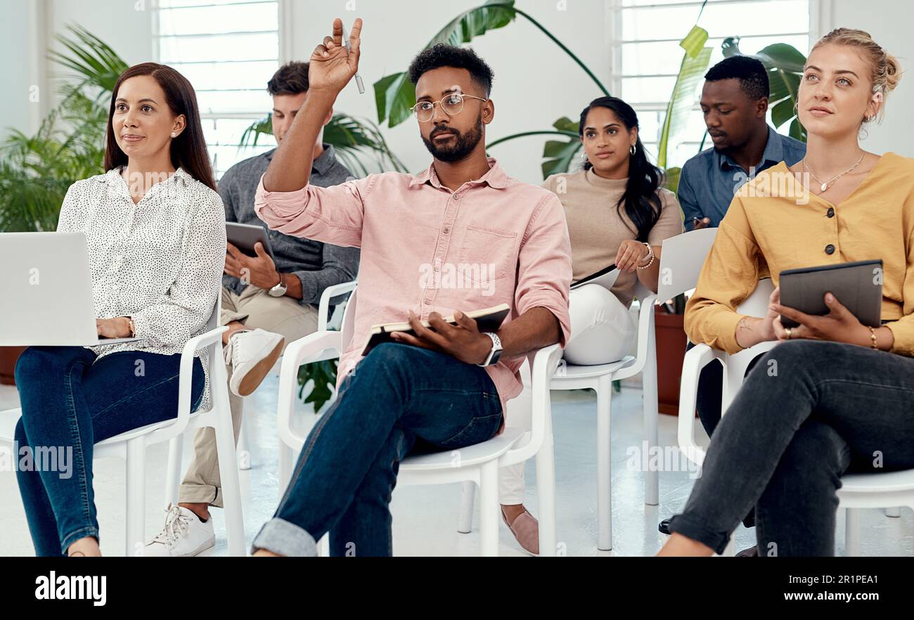 Posso fare una domanda. un bel giovane uomo d'affari seduto con i suoi colleghi e sollevando la mano durante una presentazione in ufficio. Foto Stock