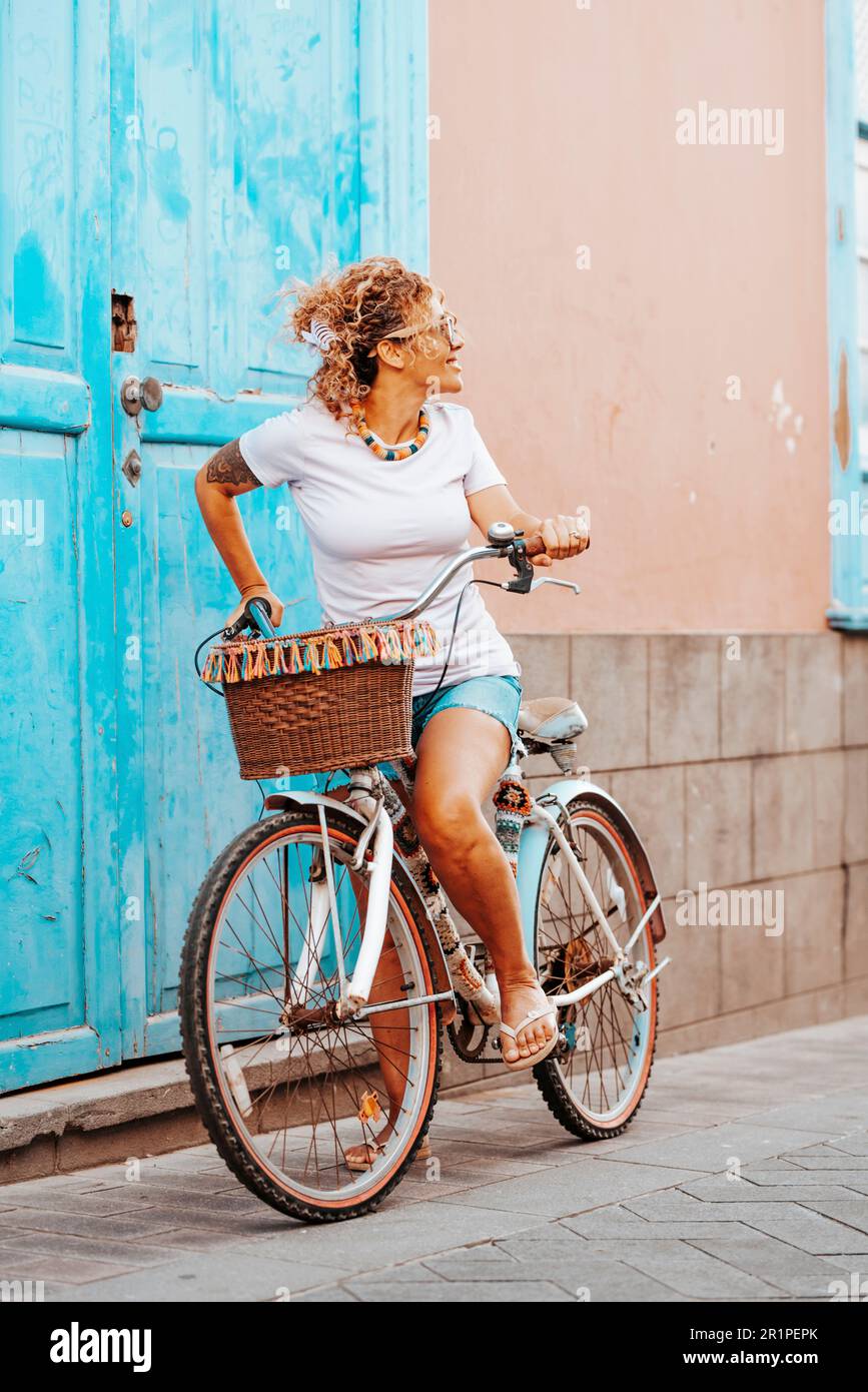 Una giovane adulta adulta adora la bicicletta da sola in strada. Casa porta blu sullo sfondo. Donna che guarda indietro e in bicicletta da sola. Primavera all'aperto attività di svago persone e concetto di trasporto Foto Stock