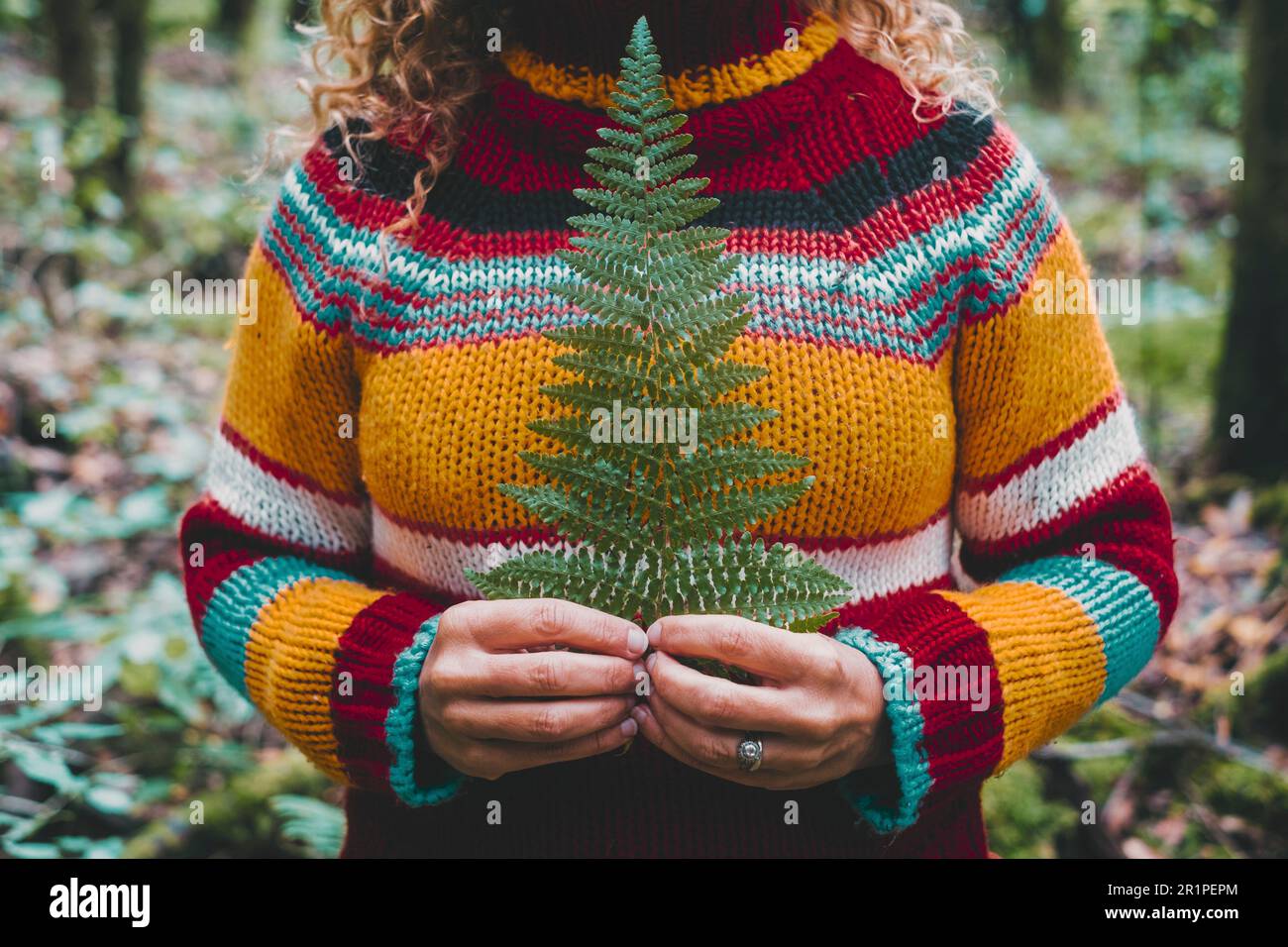 Una donna con un pullover casual colorato in lana che tiene una grande foglia tropicale. Parco naturale foresta in background. Concetto di stile di vita naturale persone che amano all'aperto. Tempo libero. Felicità e vita facile Foto Stock