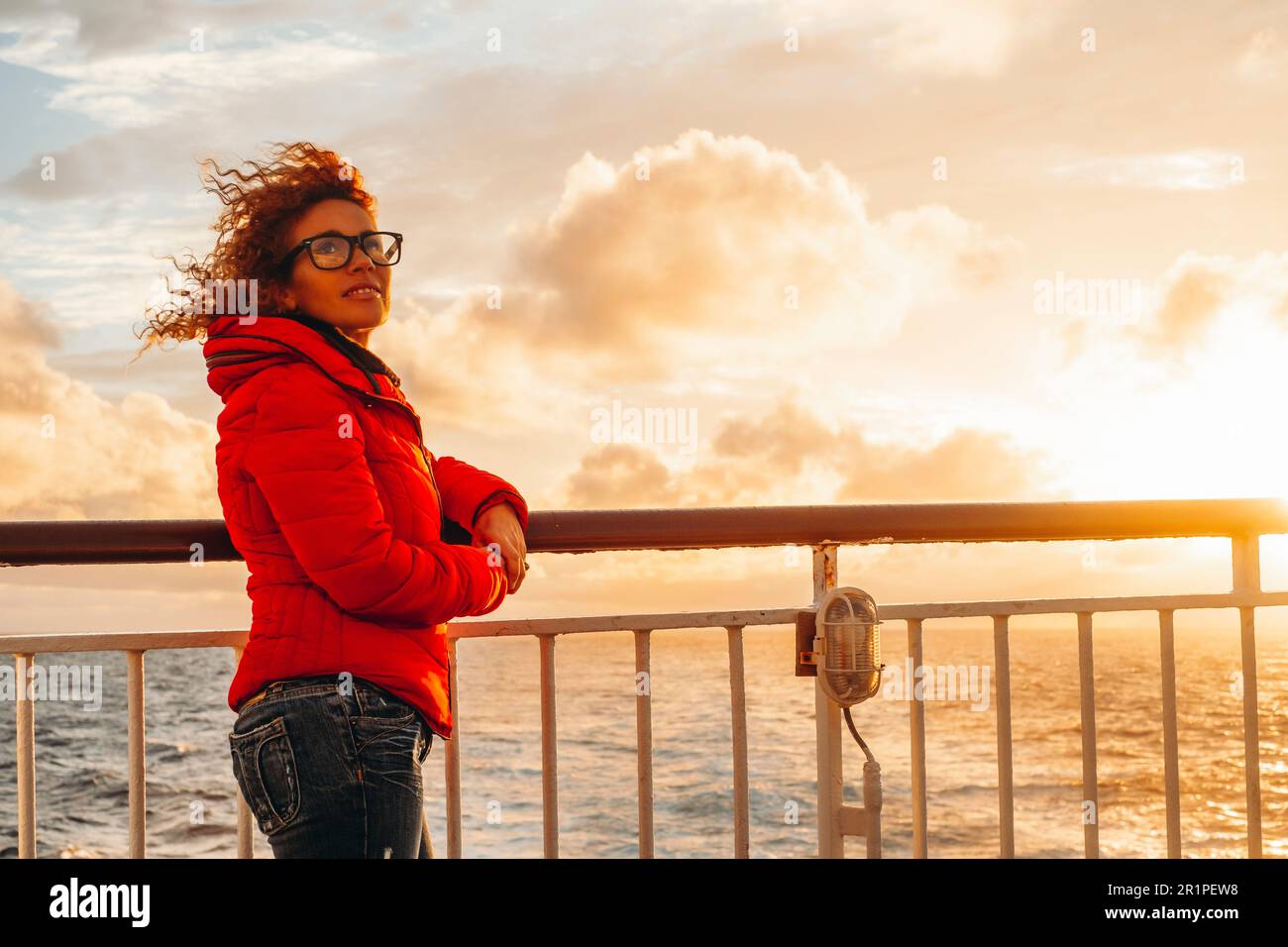 Giovane donna turistica adulta godere di caldo tramonto arancione sul molo di una nave traghetto durante le vacanze viaggio. Buon viaggiatore sull'oceano. Onde marine e orizzonte sullo sfondo. Avventura di viaggio Foto Stock