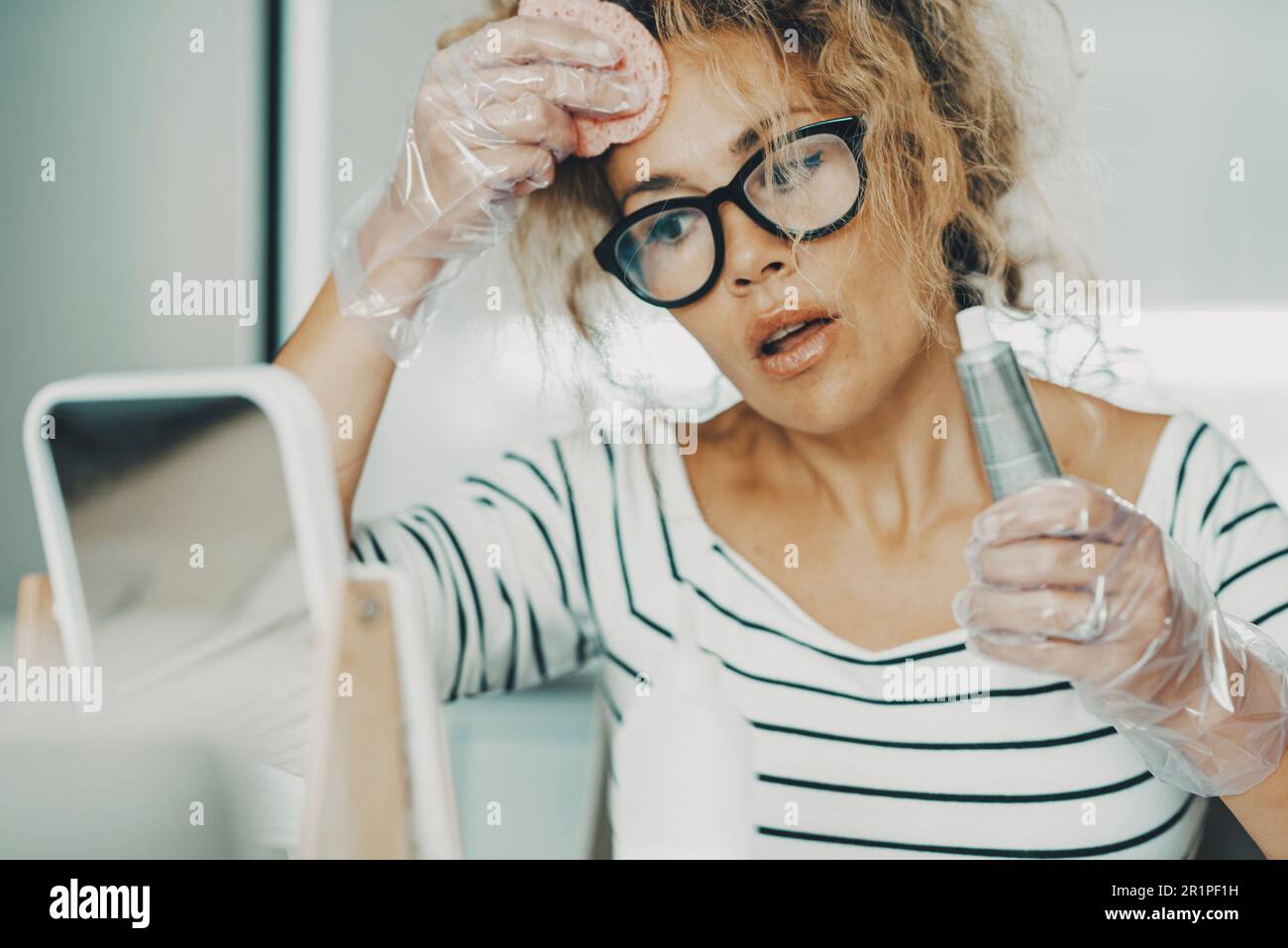 Una donna che fa tintura di acconciatura da sola a casa con gli attrezzi e il processo di cura dei capelli di salute di bellezza. Controllo dell'invecchiamento per le giovani donne adulte. donna con occhiali, prodotti chimici o naturali Foto Stock