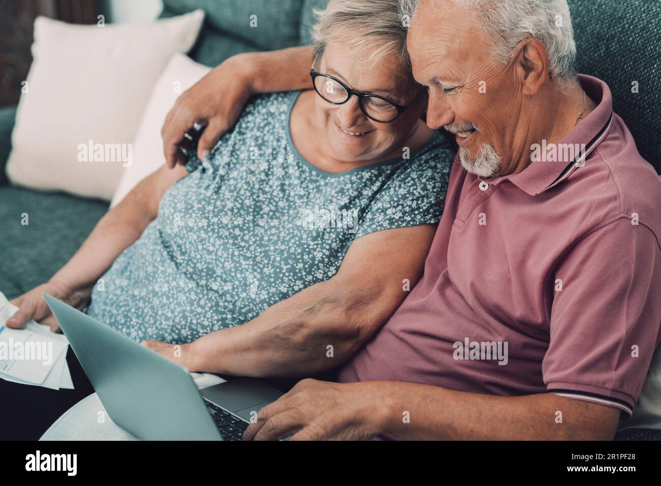 Una coppia anziana felice e jyful nel paese che gode l'attività di svago della tecnologia e del Internet insieme al laptop che si siede sul divano. Persone anziane moderne con computer che navigano sul web e si rilassano Foto Stock