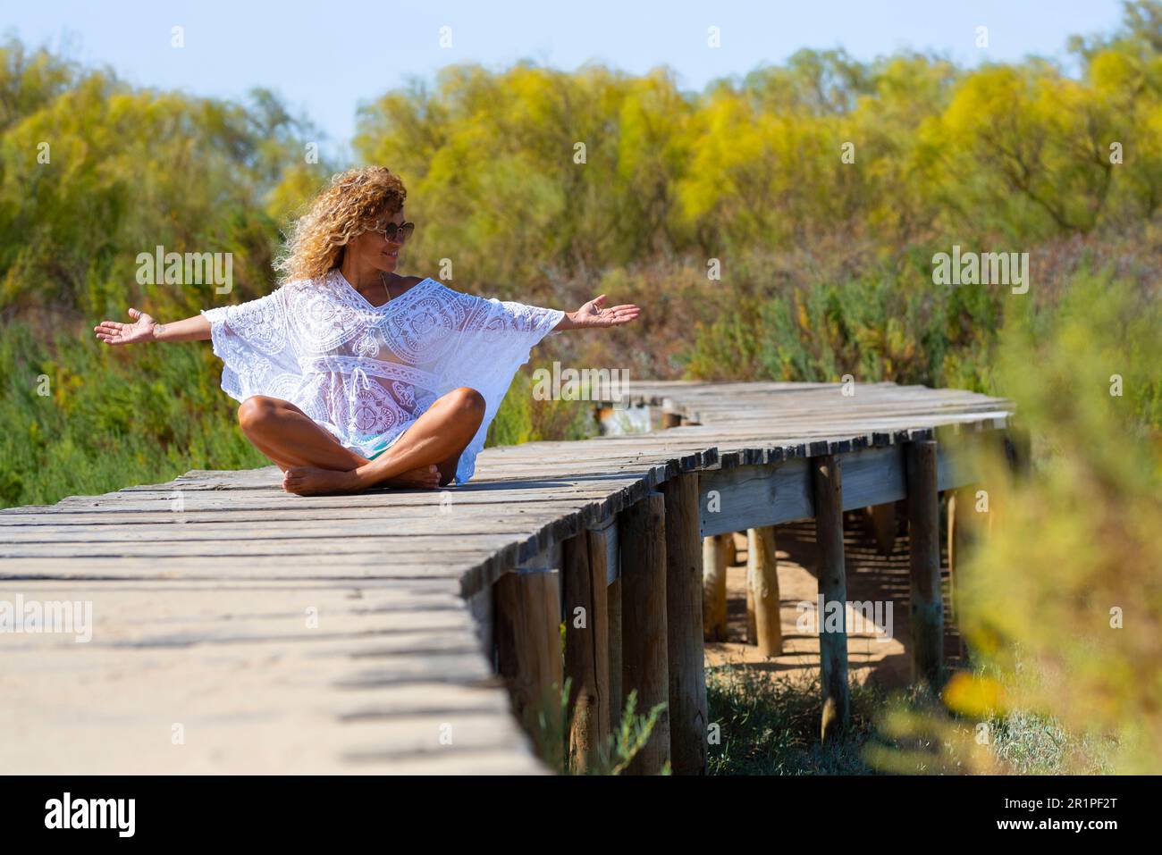 Felicità e libertà. Una donna felice e libera seduta da sola su un molo di legno al parco che apre le braccia e godendosi la sensazione. Zenlike e persone stile di vita sano. Ragazza daydreamer fuori divertirsi Foto Stock