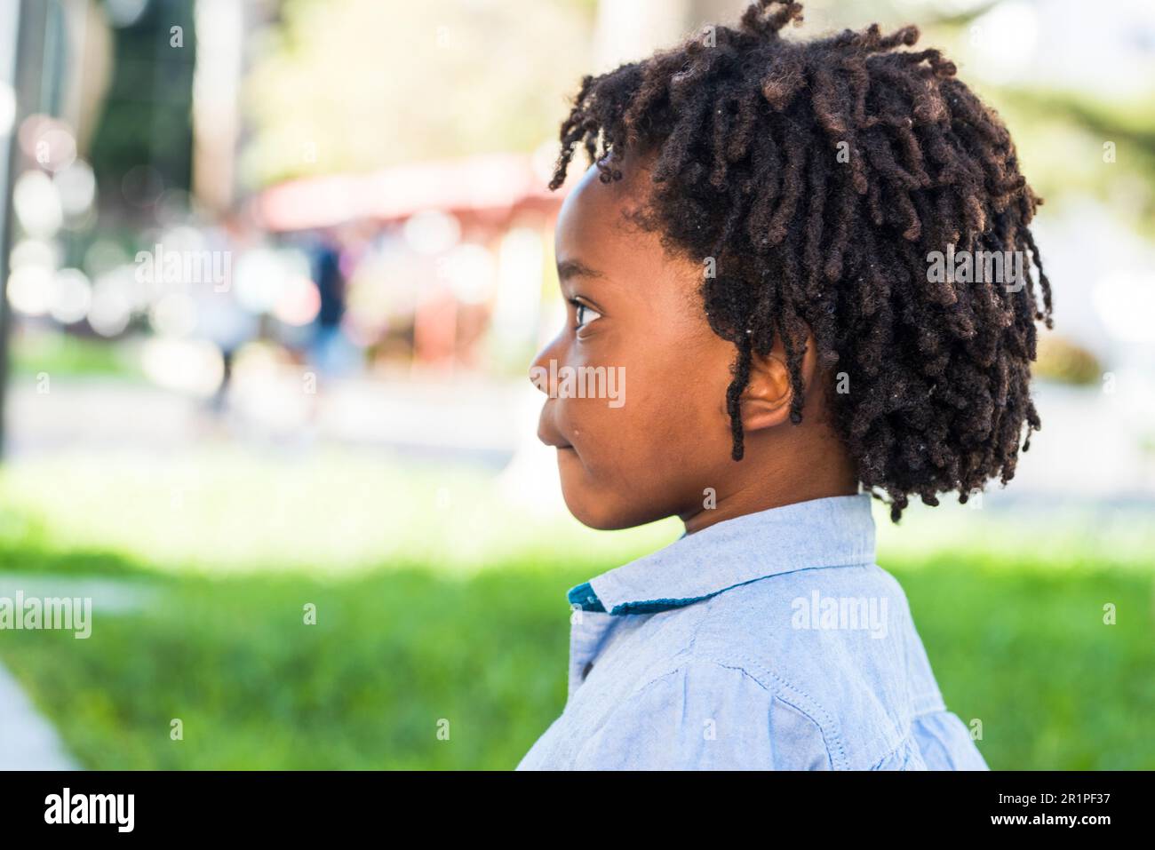 Ritratto laterale di bambini piccoli etic nero afro diversità americana con parco giochi verde sullo sfondo. Dredd capelli stile bambino solo vista laterale Foto Stock