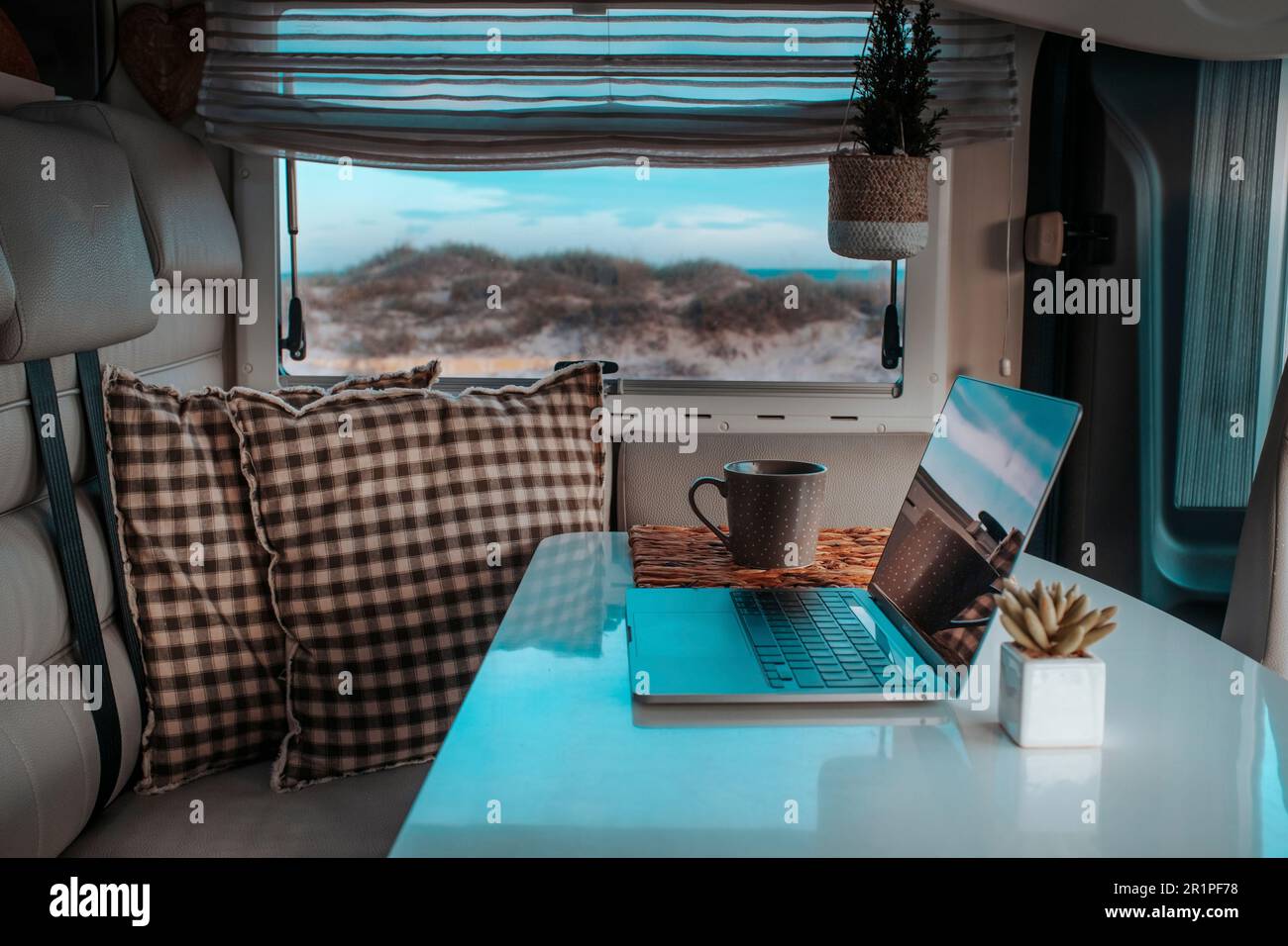 Ufficio alternativo per il lavoro intelligente e lo stile di vita nomade digitale. Un computer portatile sul tavolo del camper con una splendida vista sulla spiaggia naturale. Libertà stile di vita persone. Business del lavoro online Foto Stock