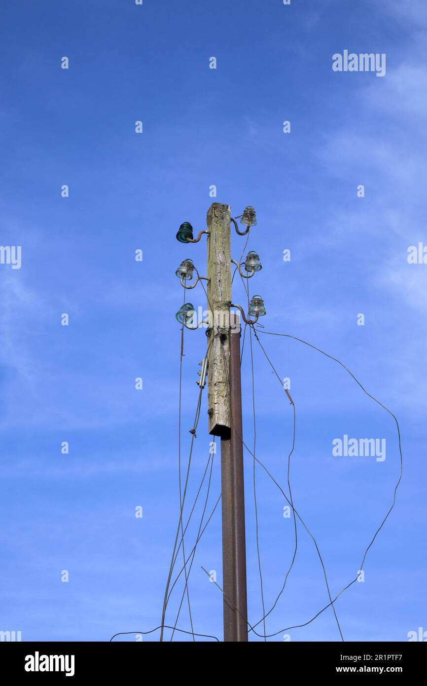 Vecchio palo telefono in disuso con cavi tagliati con cielo blu in verticale Foto Stock