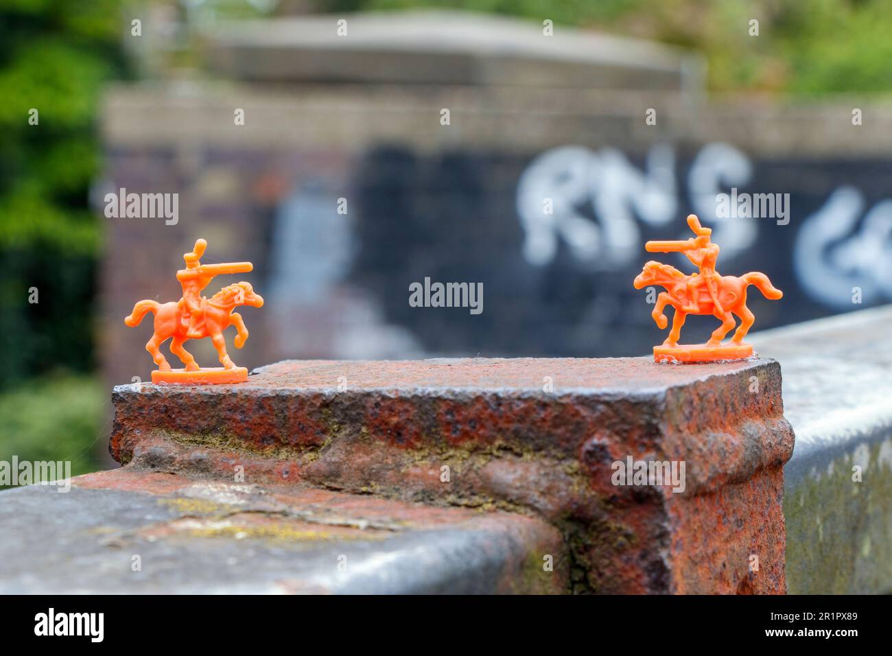 Soldati giocattolo in plastica arancione in miniatura incollato a un parapetto ponte sul sentiero maturo Parkland Walk nel Nord di Londra, Regno Unito Foto Stock