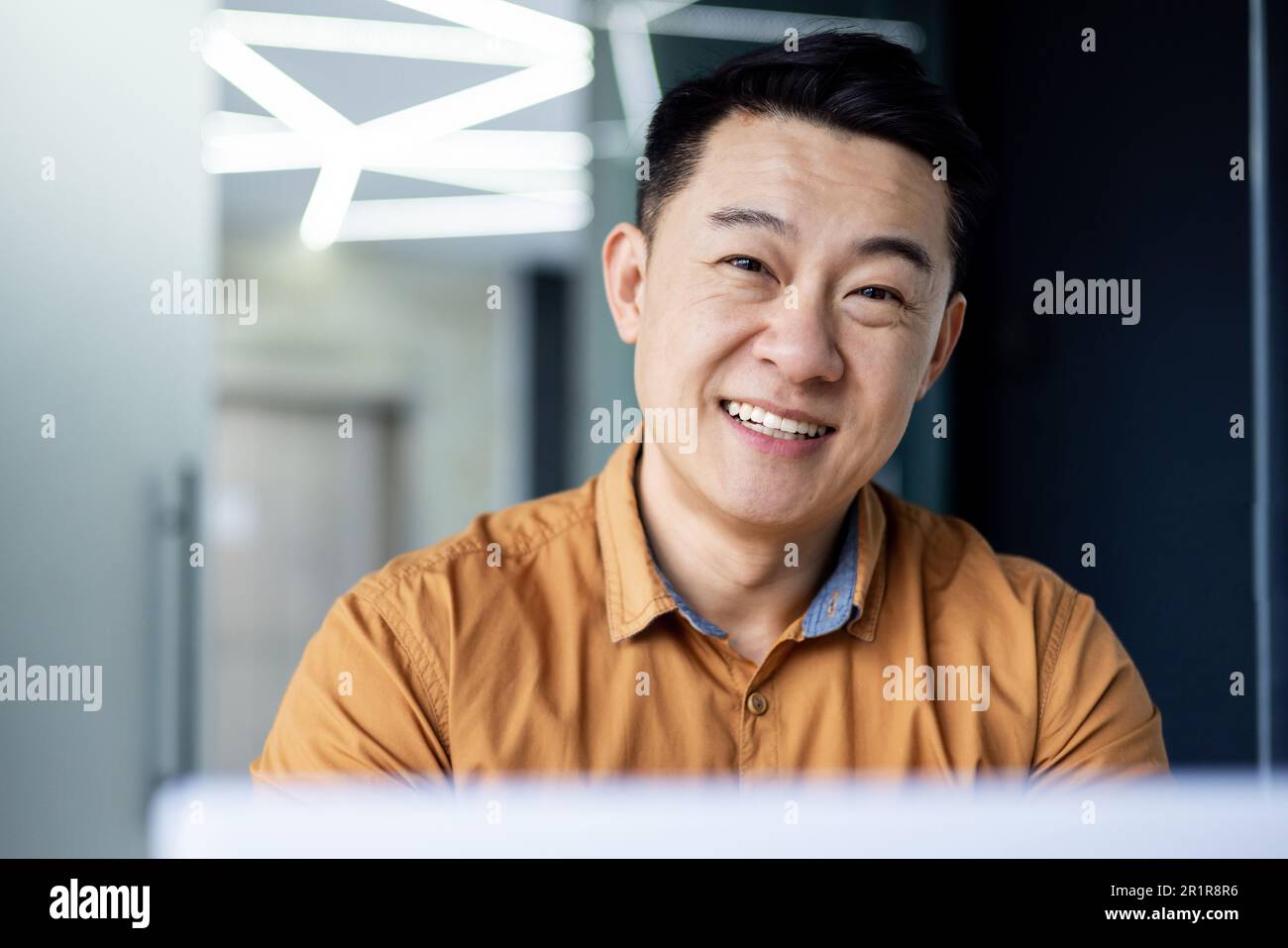 Primo piano. Ritratto di giovane uomo d'affari asiatico sorridente in camicia in ufficio moderno. Foto Stock