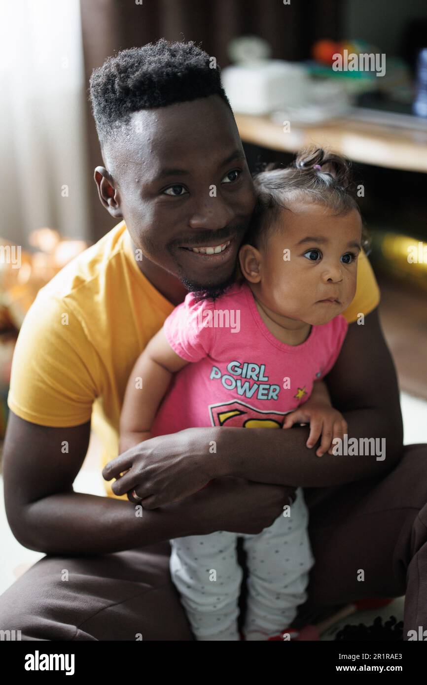Il giovane uomo africano gioca con la figlia del bambino dal matrimonio interracial nella stanza. Primo piano. Concetto di famiglia interracial. Foto Stock