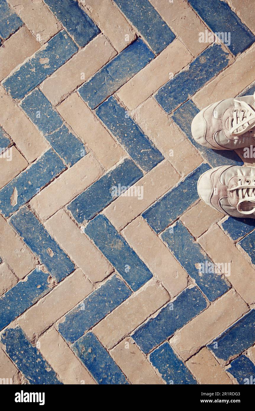 Vista dall'alto di una persona che indossa scarpe da ginnastica su un pavimento piastrellato blu e bianco Foto Stock