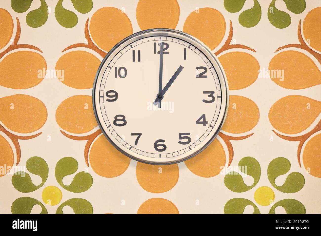 Orologio da ufficio che mostra una o'clock appeso su una parete con carta da parati vintage con motivo floreale Foto Stock