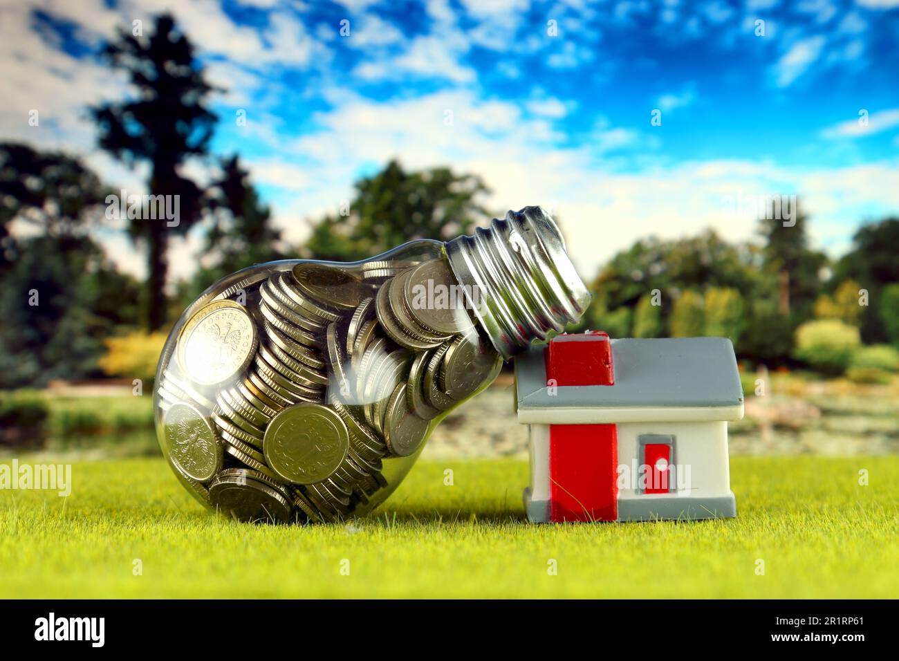 Monete all'interno della lampadina e casa in miniatura sull'erba. Eco-verde energia rinnovabile concetto. I prezzi dell'elettricità, il risparmio energetico in famiglia. Foto Stock