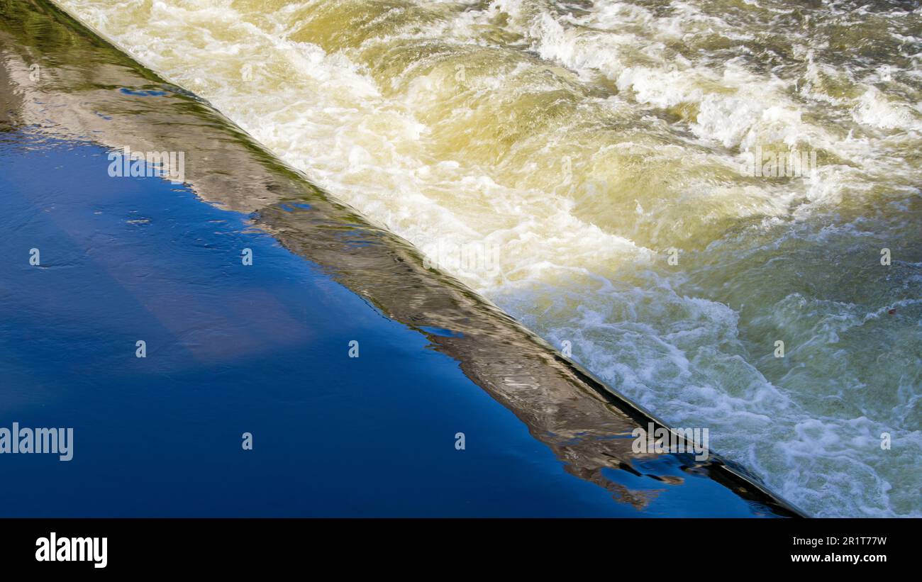 Un flusso di acqua schiumosa e una piccola sporgenza sul fiume. Foto Stock