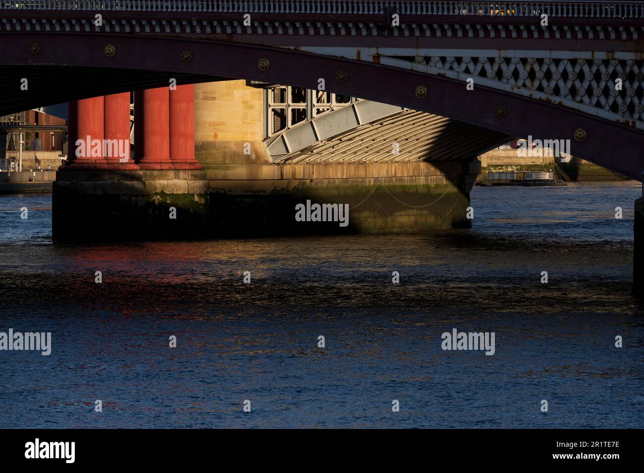 Una vista attraverso uno degli archi del ponte Blackfriars Road attraverso il Tamigi, di un pilastro illuminato dal sole del ponte della ferrovia Blackfrairs. Nero Foto Stock