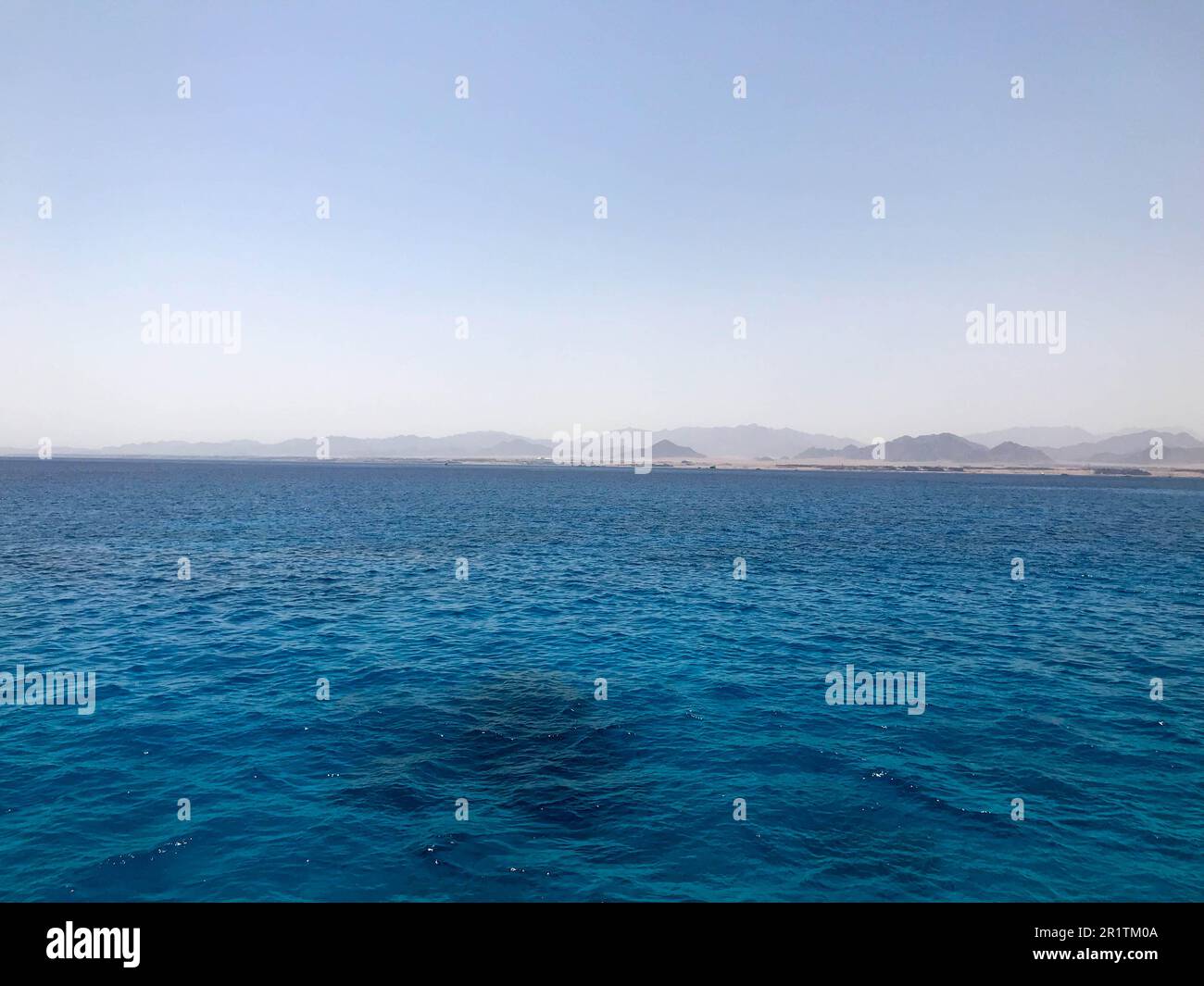 Paesaggio di acqua salata, mare, mare, oceano con onde, increspature sotto il sole bruciante sullo sfondo di montagne lontane Foto Stock