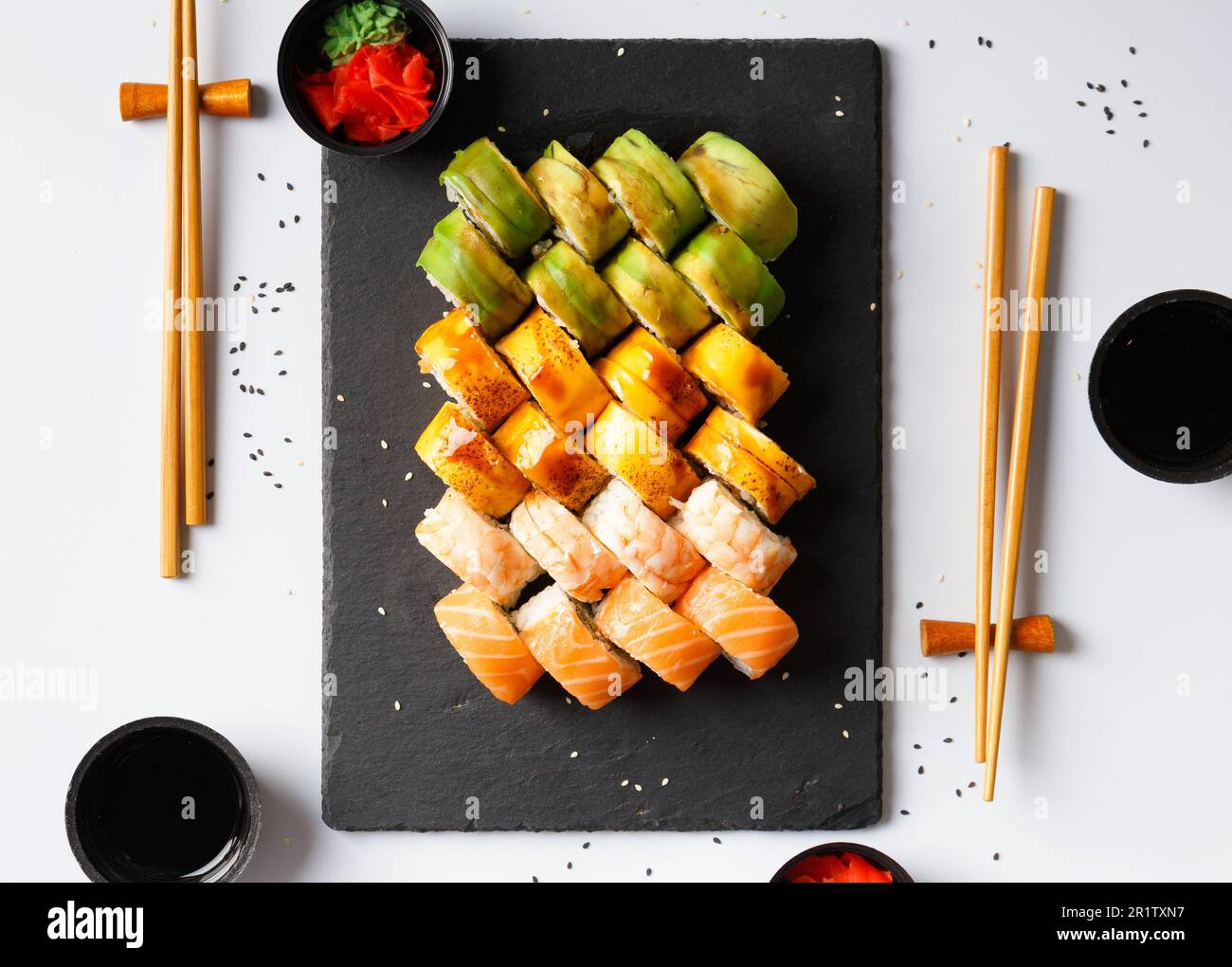 Set di involtini colorati con gamberi, salmone, avocado, formaggio, zenzero sottaceto, wasabi, salsa di soia, bastoncini cinesi su sfondo bianco, vista dall'alto. Foto Stock