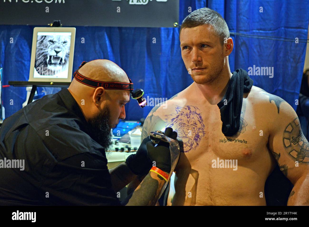 Un artista tatuaggio che lavora sul petto di un uomo muscoloso al New York City Tattoo Convention al Roseland Ballroom di Midtown Manhattan, NY Foto Stock