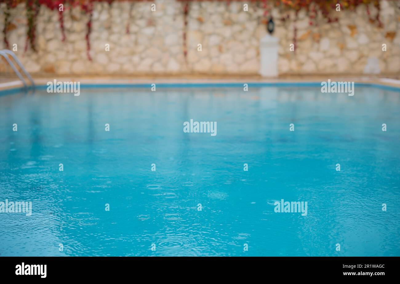 Piscina all'aperto con tempo piovoso, stagione piovosa, sfondo estivo astratto e sfocato per la festa in piscina dell'hotel resort, idea screensaver Foto Stock