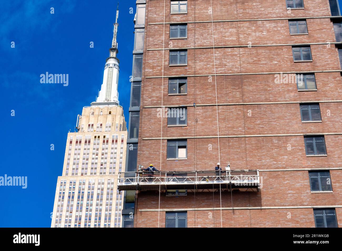 I lavoratori conducono il rimointing dei mattoni su una piattaforma sospesa con l'Empire state Building sullo sfondo, 2023, New York City, Stati Uniti Foto Stock