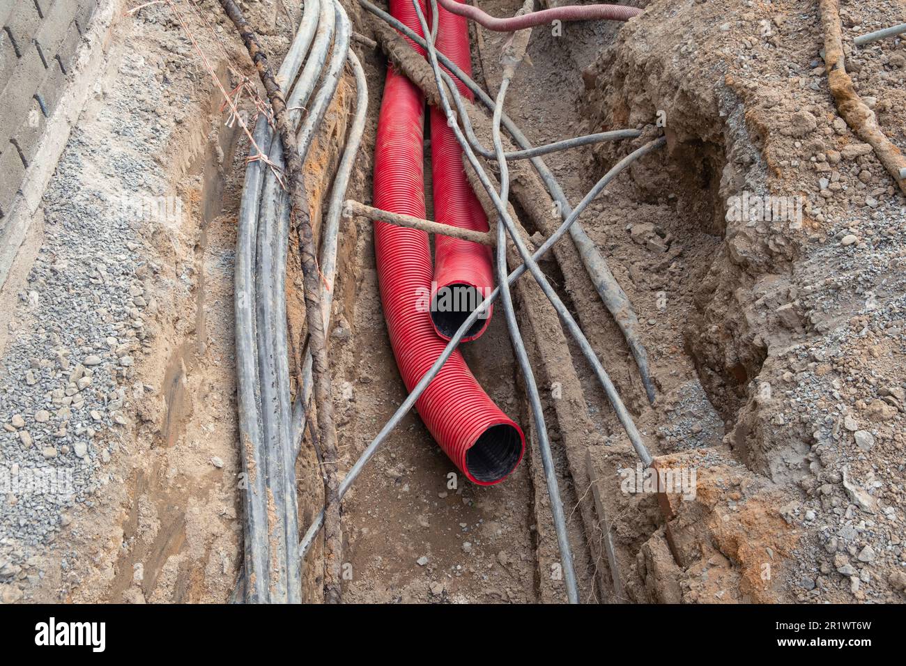 Il tubo corrugato rosso è sepolto sottoterra sulla strada fatta per  l'installazione di infrastrutture di cavi elettrici. Cantiere con molta  fornitura e Foto stock - Alamy