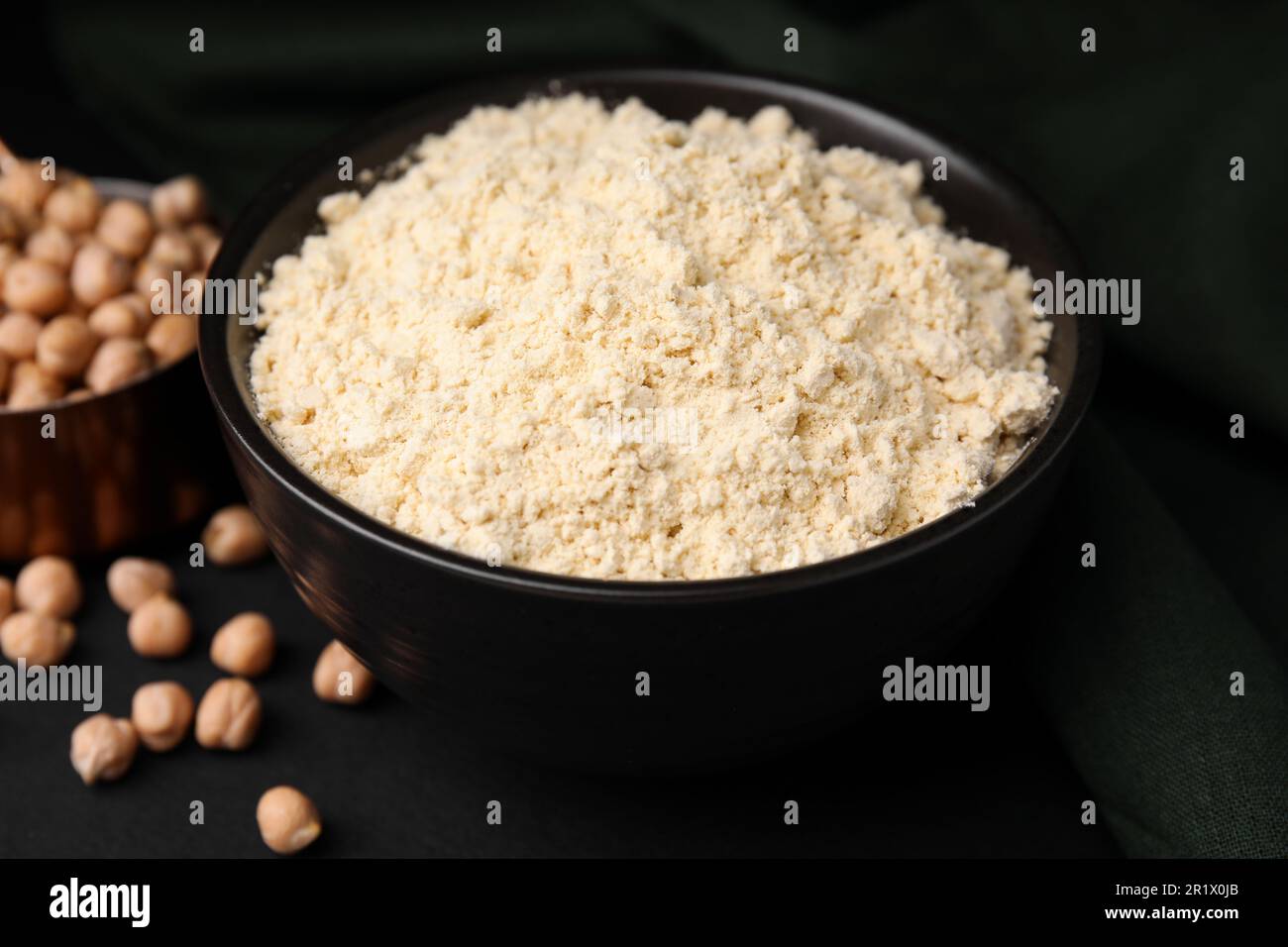 Farina di ceci in ciotola e semi su tavola nera Foto Stock