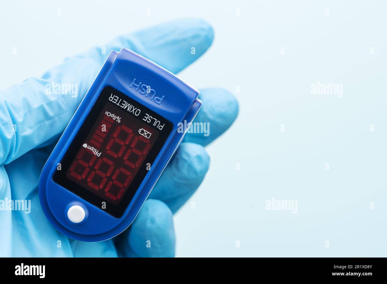 Pulsossimetro in mano del medico con guanto su sfondo blu. Una mano in un guanto medico contiene un dispositivo per la diagnostica sanitaria Foto Stock