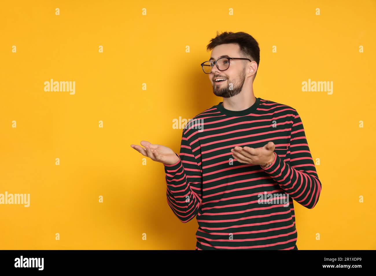 Bell'uomo in felpa a righe gesturante su sfondo giallo Foto Stock