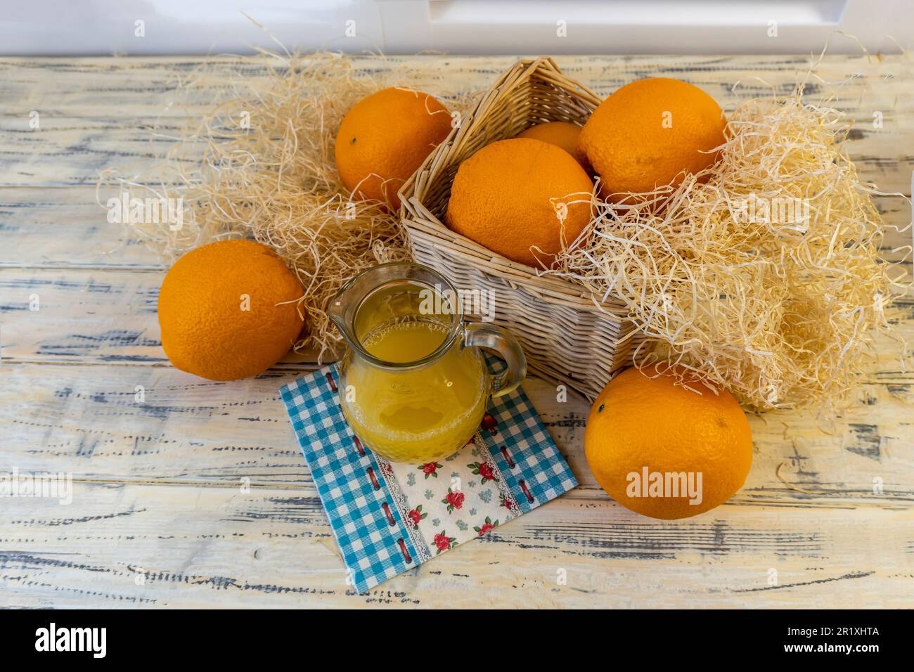Vita morta con arance, cesto e brocca di vetro con succo su vecchio sfondo di legno luminoso Foto Stock