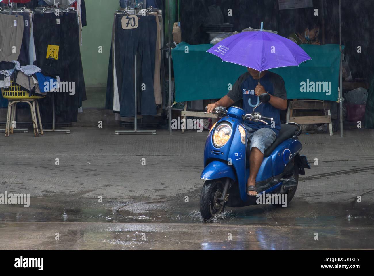 SAMUT PRAKAN, THAILANDIA, 10 2023 MAGGIO, Un motociclista guida una moto con ombrello in una mano Foto Stock