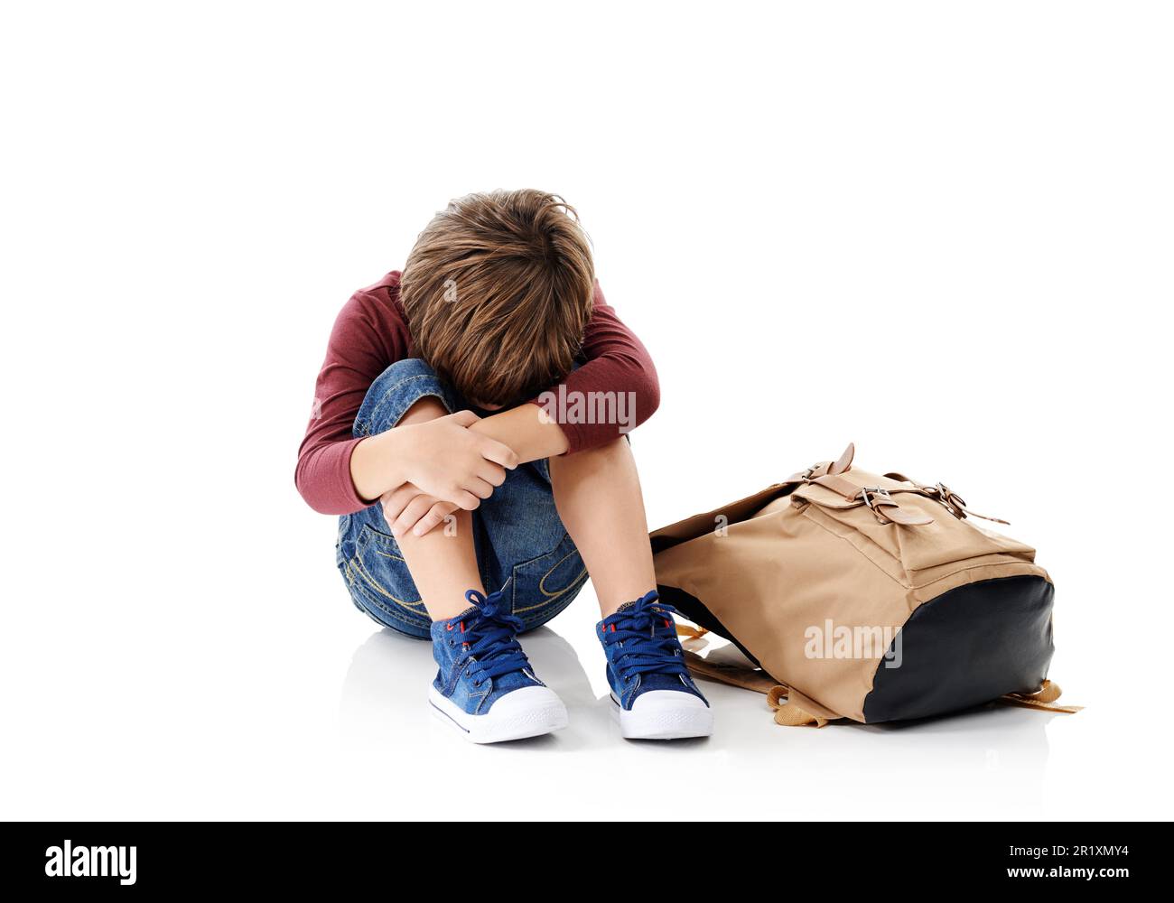 Il primo giorno di scuola può essere impegnativo. Studio shot di un ragazzino con la testa sepolta nelle ginocchia seduto accanto alla sua borsa contro un Foto Stock